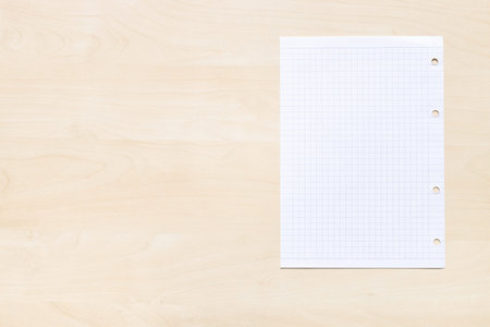 top view of blank sheet of squared paper on light brown wooden board with copyspace