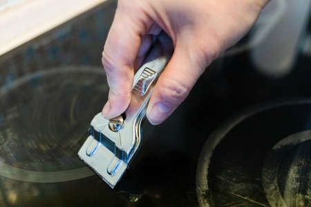 cleaning dirty surface of black ceramic hob from burnt food with steel scraper close upの写真素材