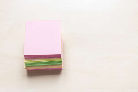top view of stacks of blank colorful sheets of note paper on light brown wooden board with copyspaceの写真素材