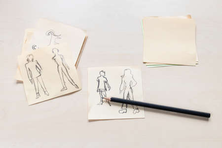 sketches of fashionable silhouette of woman of the XX century hand drawn by black pencil on sheets of paper on light brown tableの写真素材