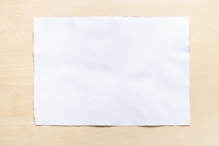 top view of blank sheet of white textured watercolor paper on light brown wooden board