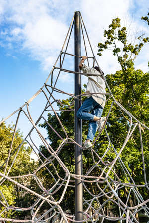 girl climbs on rope playground in city courtyard on sunny dayの写真素材