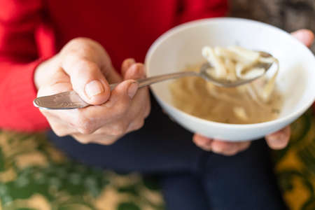 hand of old woman holds tablespoon of chicken noodle soup (focus on the upper foreground thumb)の写真素材