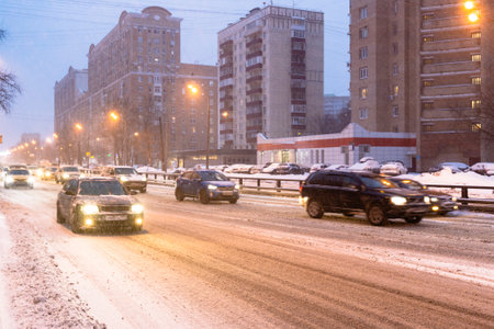 traffic on slippery snowy city road in snowfall in pink winter twilight in Moscow cityの写真素材