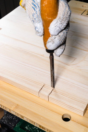 carpenter using chisel cuts groove on wooden board close up at home