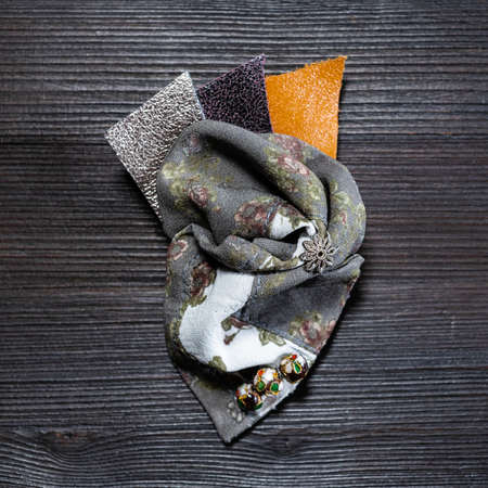 top view of handcrafted silk and leather brooch decorated with cloisonne beads on dark wooden boardの写真素材