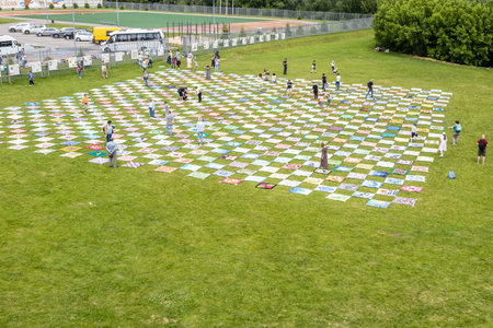 Kolomna, Russia - June 11, 2022: above view of handmade patchwork quilts on green meadow during...
