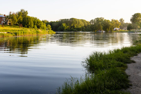calm surface of Kolomenka river and view of urban beach in Kolomna city at summer sunset