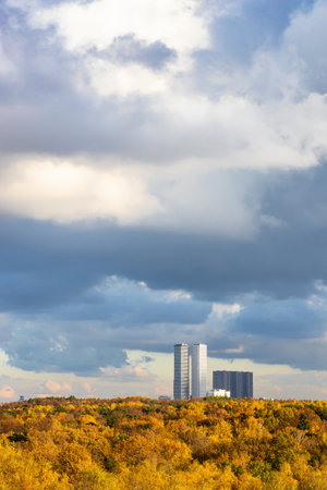 large rainy cloud over yellow autumn forest and skyscrapers on horizon on sunny dayの写真素材
