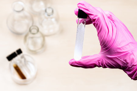 hand holds closed test-tube with white translucent liquid over light desk with flasks