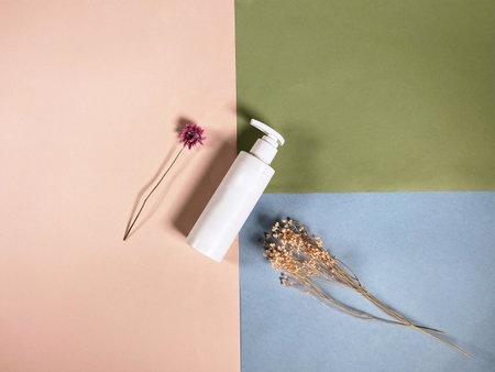 top view of white blank pump plastic bottle and natural dried plants on color paper backgroundの写真素材