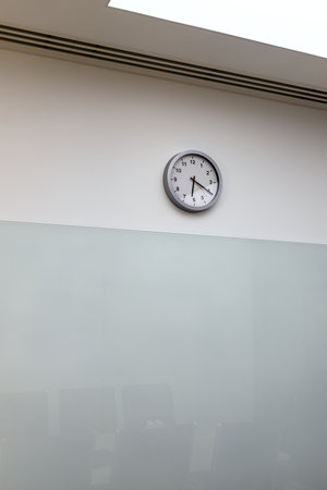 clock on wall of empty office hall shows twenty past six after end of working dayの写真素材