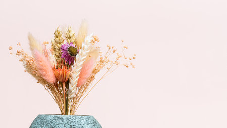 flowers and dried spikelets in ceramic vase on pink background with copyspaceの写真素材