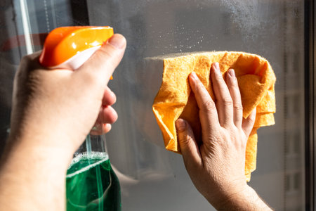 cleaning outdoor home window glass in urban house close up on sunny spring day (focus on hand with...