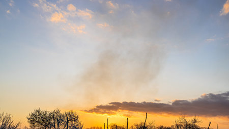 panoramic view of sunset sky with smoke from campfire in spring evening
