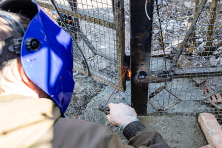 welder welds hinge to freshly concreted gate post in village outdoors