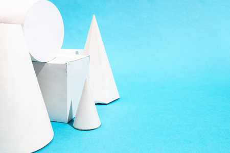 several hand-crafted paper geometric objects close up on turquoise blue background with copyspaceの写真素材