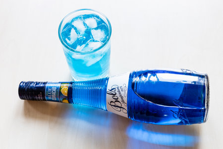 Moscow, Russia - August 2, 2022: above view of lying blue Curacao liqueur made by Bols distillery, founded in 1575 in Amsterdam, on pale table and glass with Blue Lagoon cocktailのeditorial素材