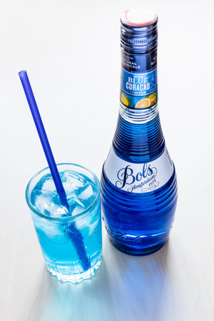 Moscow, Russia - August 2, 2022: above view of blue Curacao liqueur made by Bols distillery, founded in 1575 in Amsterdam, on pale table and glass with drinking straw and Blue Lagoon cocktailのeditorial素材