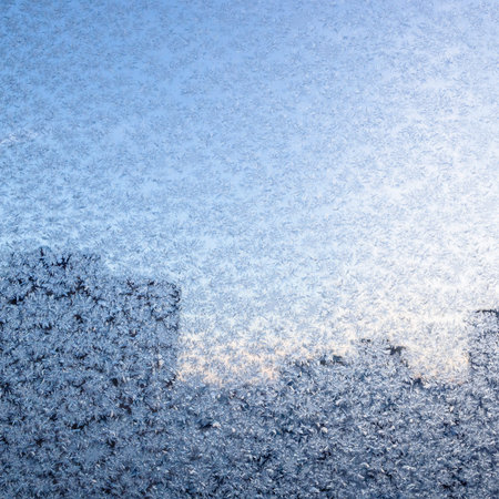frosty pattern on home window glass and silhouette of high-rise city houses in background on cold...