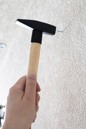 male hand with hammer drives nail into white wall iat homeの写真素材