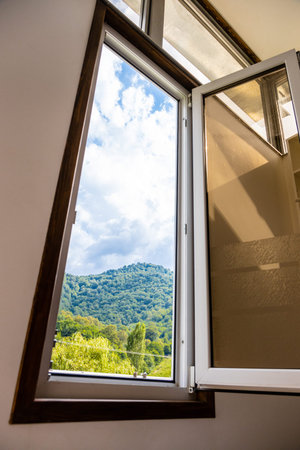 view of cloudy sky over overgrown mountain through home window on sunny summer day in Dilijan city,...