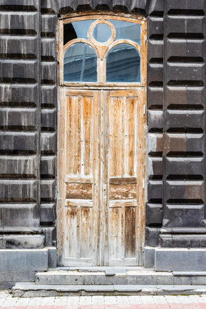 old shabby wooden door in old house from black tuff stone on street in Gyumri city, Armrnia on overcast summer dayの写真素材