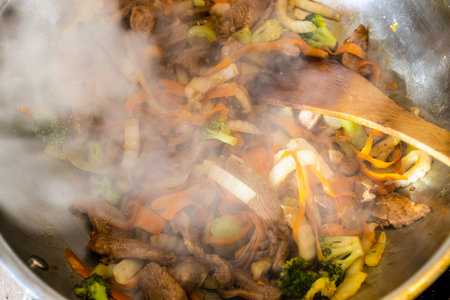 stirring of frying turkey meat and vegetables in wok with wooden spatula at home kitchenの写真素材