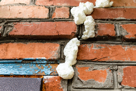 fresh construction foam filled cracks in brickwork in the wall of village barn close-upの写真素材
