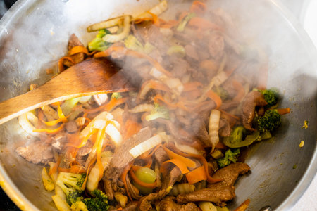 mixing of frying turkey meat and vegetables in wok with wooden spatula at home kitchenの写真素材