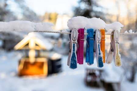 snow-covered clothespins on clothesline closeup in country yard with well in sunny winter eveningの写真素材
