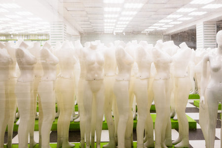 view through outside window glass of many full body dress mannequins in hall of closing clothing...