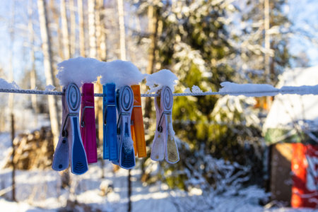 clothespins on clothesline covered with snow close-up in yard of rural house on sunny winter dayの写真素材