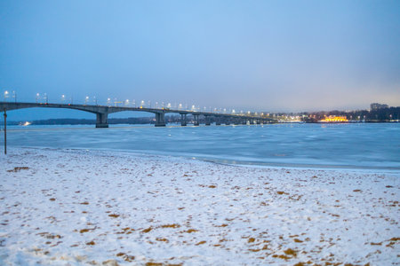 bank of frozen river and bridge in Kostroma city in blue winter evening twilightの写真素材