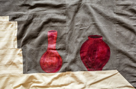 fragment of handcrafted textile panno with handpainted red jug and vase on tableの写真素材