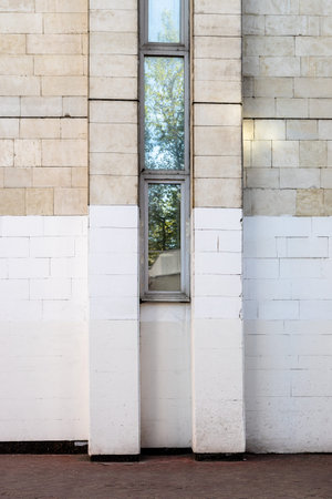 brick wall of city house painted white from below with narrow window on spring day