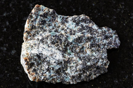 sample of raw gabbro-norite mineral on black granite background close up from Karelia, Russia