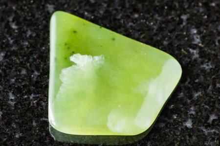 sample of polished light green nephrite mineral on black granite background close up from Sayan...
