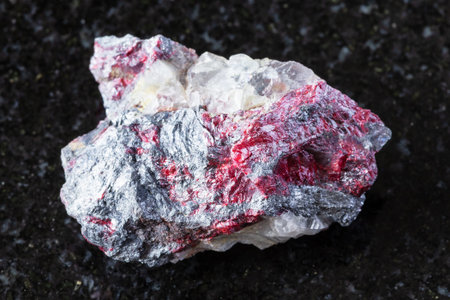 sample of raw cinnabar and stibnite on fluorite mineral on black granite background close up from...