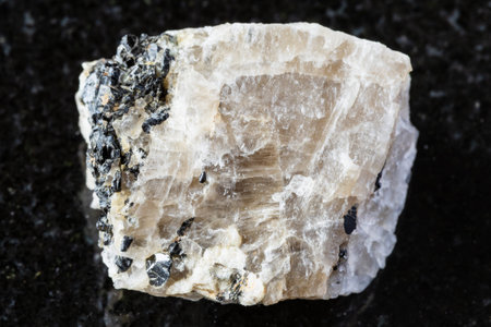 sample of raw cryolite mineral with annite mica on black granite background close up from Eastern...