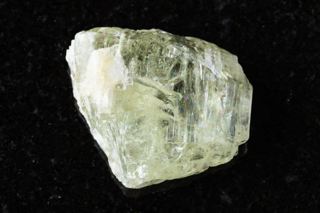 sample of raw hiddenite mineral on black granite background close up from Brazil