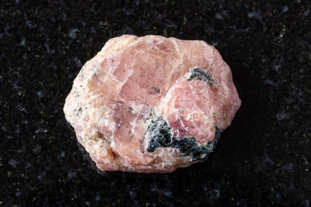 sample of raw pink ruby mineral on black granite background close up