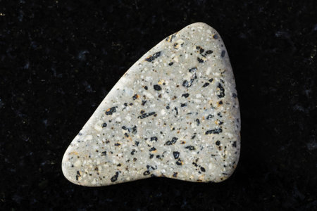 sample of polished andesite mineral on black granite background close up from Crimea