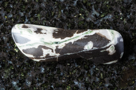 sample of tumbled hornfels mineral on black granite background close up from Khakassia, Russia