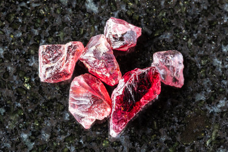 sample of several raw pyrope crystals on black granite background close up from Tanzania