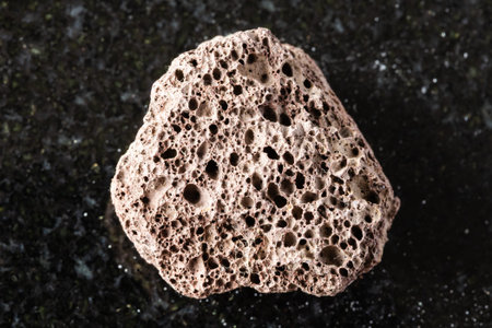 sample of rough brown pumice mineral on black granite background close up