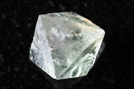 sample of single raw fluorite crystal on black granite background close up