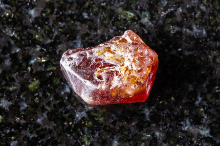 sample of raw hyacinth zircon crystal on black granite background close up from Tanzania