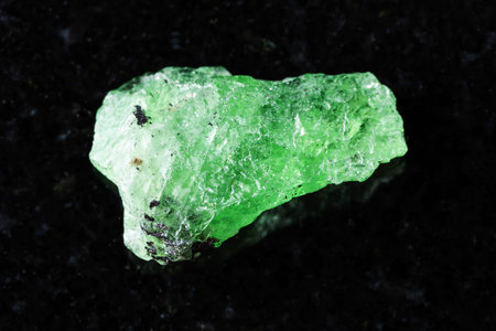 sample of raw tsavorite garnet mineral on black granite background close up from Tanzania