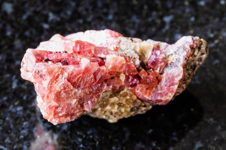 sample of rough rhodonite rock on black granite background close up from Brazilの写真素材